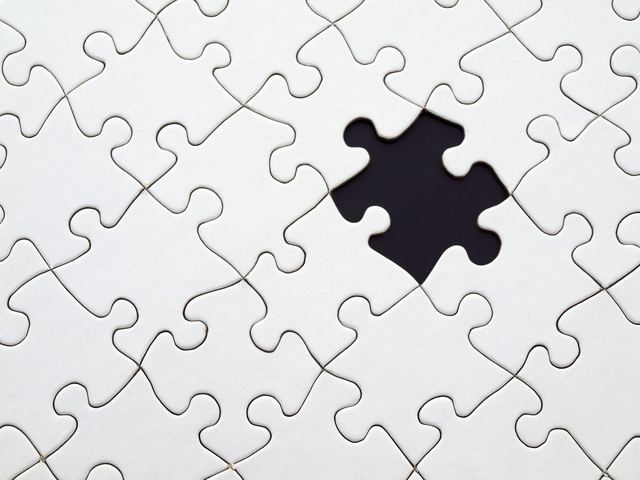 Puzzle incomplet auquel il manque une seule pièce Puzzle presque terminé sur une table, avec un espace vide là où manque une pièce